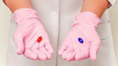 Pessoa com luvas segurando uma pílula azul e outra vermelha
