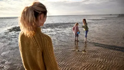 Mulher olhando duas meninas brincando na praia
