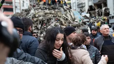 A woman in tears with a mound of rubble behind her.