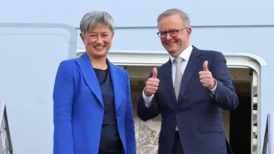 Anthony Albanese gives a thumbs up while boarding a plane beside Penny Wong