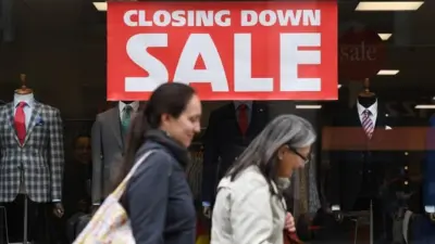 People walk past closing down sign in shop window.