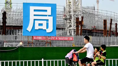 A man and children cycle past the Guangzhou FC football stadium, which is being built by Evergrande.