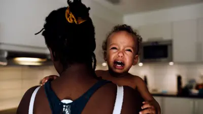በእናቷ እቅፍ ውስጥ ሆና የምታለቅስ ሕጻን