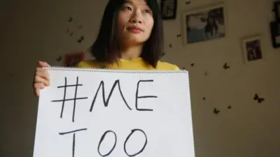 Huang standing with a Mee Too placard