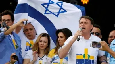 Fotografia colorida mostra Bolsonaro na Marcha para Jesus em frente a uma bandeira de Israel