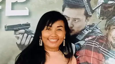 Lily Naing Kyaw posing in front of a poster of a military propaganda film