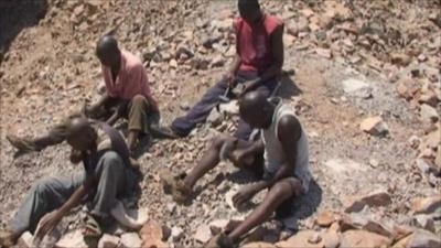 Men in the search for diamonds using hammers on rocks.