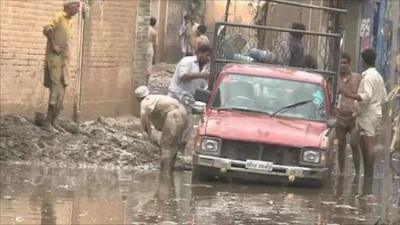 Men digging car out of flooded muddy street