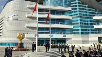 Officials gather with bowed heads around flags at half-mast in Bauhinia Square in Hong Kong