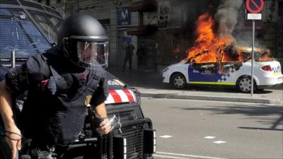 A riot police runs as a patrol police car burns during riots in Barcelona