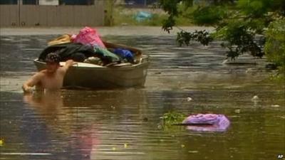 Man dragging boat of his possessions through flood water