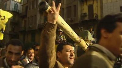 Protesters march past a tank