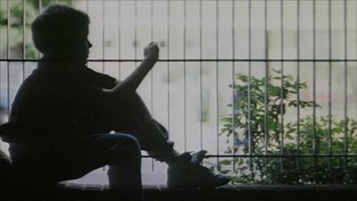 A teenage boy sitting in front of a metal fence