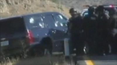 Police officers look at car with bullet holes