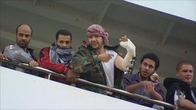 A group of men, one with a bandaged arm, arrive on a ship arriving in Benghazi