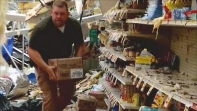 Man moving boxes in his badly damaged shop