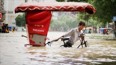 Man in China pushing cart through flood waters