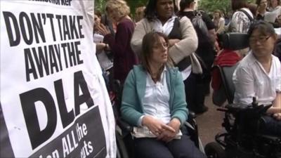 Protesters beside placard defending the disability living allowance