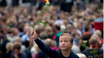 A boy holds up a rose at a memorial vigil in Norway