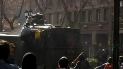 Protester climbing on tank fitted with water cannon