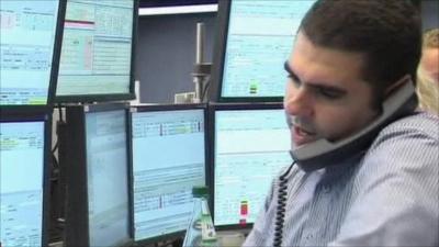 Man on phone in front of market screens