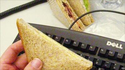 Man holding a sandwich over his computer keyboard