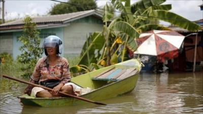 A woman wears a helmet as she maneuvers a small boat through a flooded area in Ayutthaya province