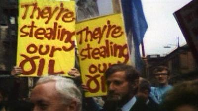 Protestors carry placards as Harold Wilson walks past