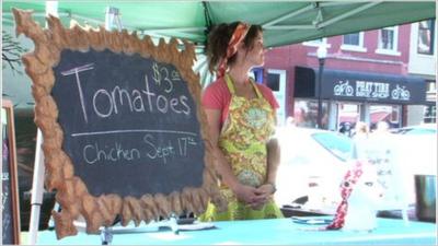 A farmer standing near a sign advertising organic tomatoes