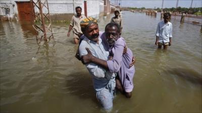 Residents assist a handicapped man while escaping to higher ground from their flooded village in the Mirpur Khas