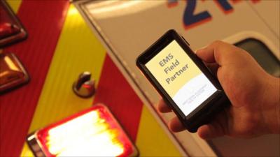 A hand holding a mobile in front of an ambulance