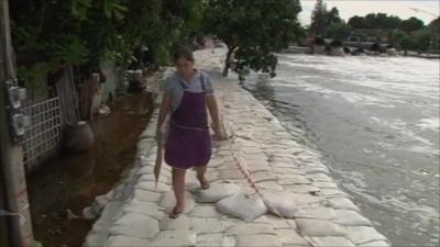 Woman walking along dam made of sandbags next to swollen river