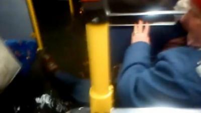 Bus passenger lifts foot away from floodwater