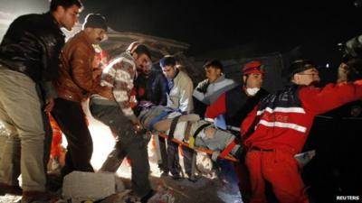 An earthquake survivor is carried by rescue workers from a collapsed building