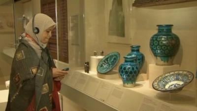 Woman listening to audio guide in front of Islamic art display