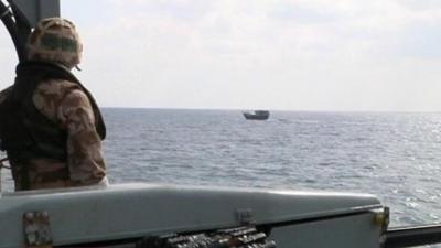 Military personnel on ship watching over small ship in sea