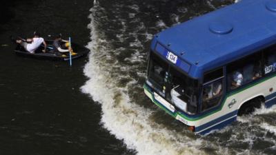 Residents travel on a boat as a bus drives on a flooded street in Bangkok