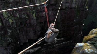 Man climbing on rope to a sea stack