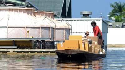 Thai factory workers using a small boat to move goods across flood water