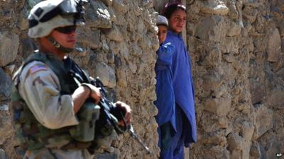 US Soldier (L) stands next to Afghan Children in a doorway (R)