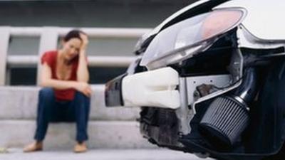 A woman sitting on the kerb with her head in her hands near the smashed front bonnet of a car.