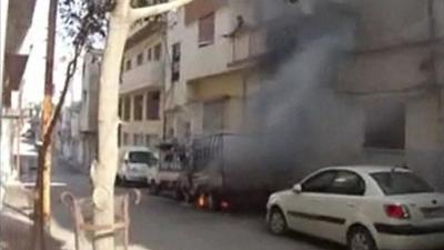 Vehicles on fire in front of apartment building in Syria