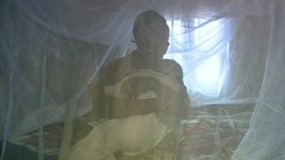 A woman sits under a malaria net with her baby
