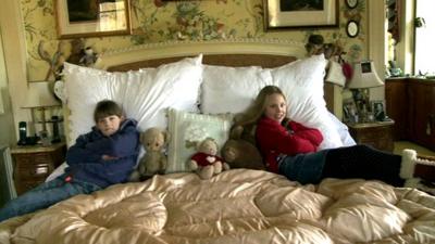 Twins Octavia and Merlin sit on a big bed.