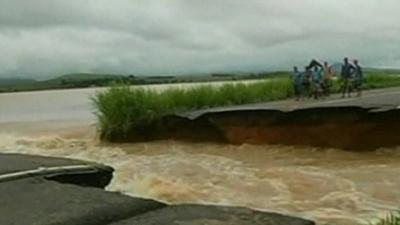 People standing on edge of road destroyed by the force of the flood