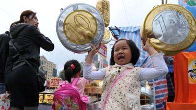 A girl holds up cushions shaped as euro and Hong Kong coins at the Chinese New Year flower market in Hong Kong