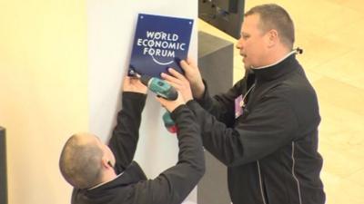 Workmen fixing a World Economic Forum sign to the wall