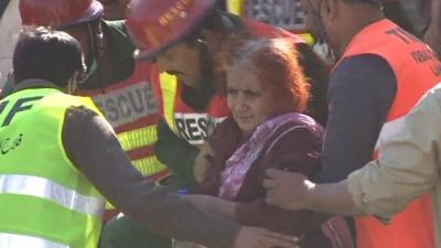 Rescue workers help a 65-year-old woman out of the rubble of the collapsed Lahore factory