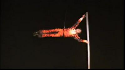 Man in tiger suit spins horizontally around a vertical pole.