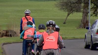 Adult cyclist leading 4 young cyclists on a road